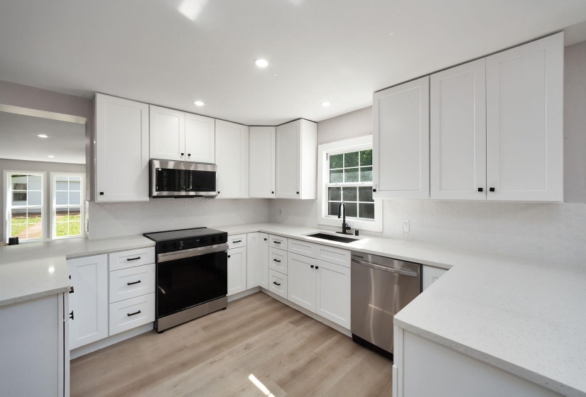 U-shaped kitchen featuring white shaker cabinetry, stainless steel appliances, light-toned countertops, wood-finish flooring, and recessed lighting