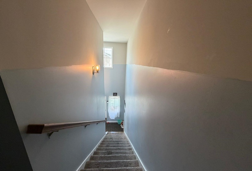 Stairwell with two-tone wall paint, a dark wood-finish handrail, and a wall-mounted light fixture