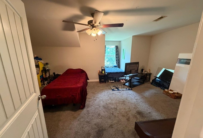 Carpeted room with a ceiling fan, sloped ceiling, and window with dark patterned curtains