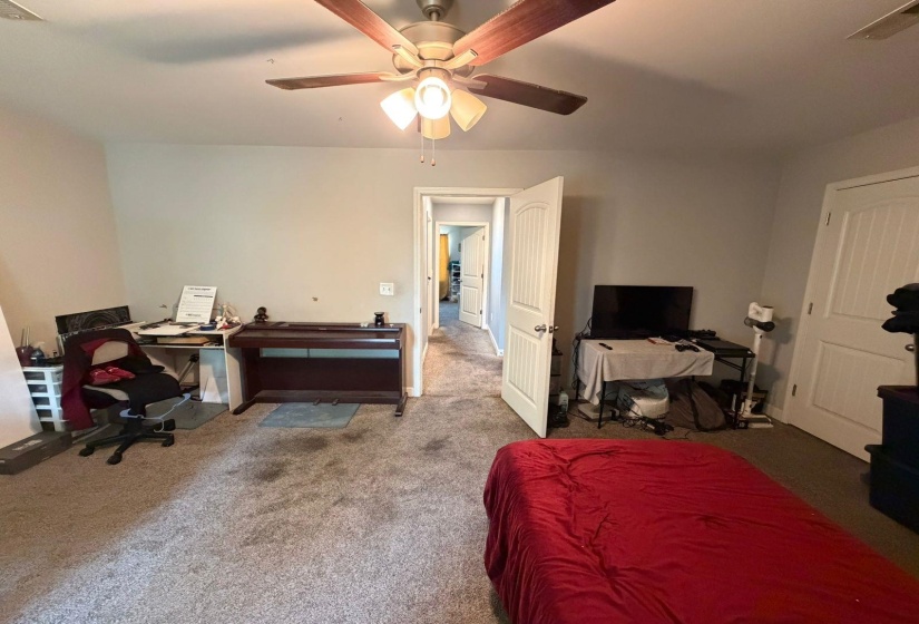 Carpeted interior space featuring a ceiling fan with light fixture, neutral wall paint, and white paneled doors