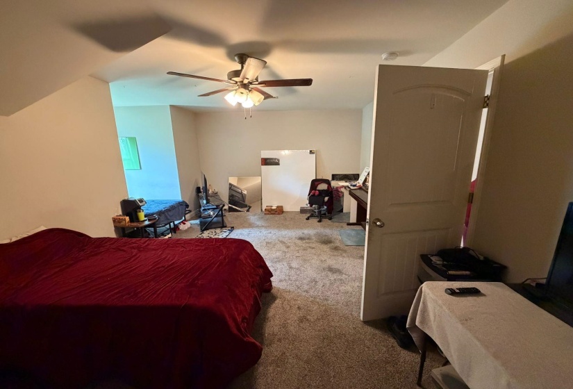 Carpeted room with a ceiling fan, sloped ceiling accents, and a white interior door with an arched panel design
