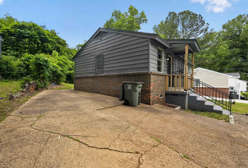 Exterior featuring gray siding, a brick foundation, a front porch with wooden posts, and concrete steps with a black metal handrail
