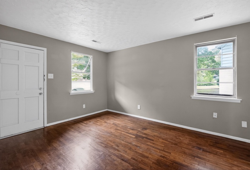 Room featuring wood-finish flooring, two windows with white trim, and a paneled white door