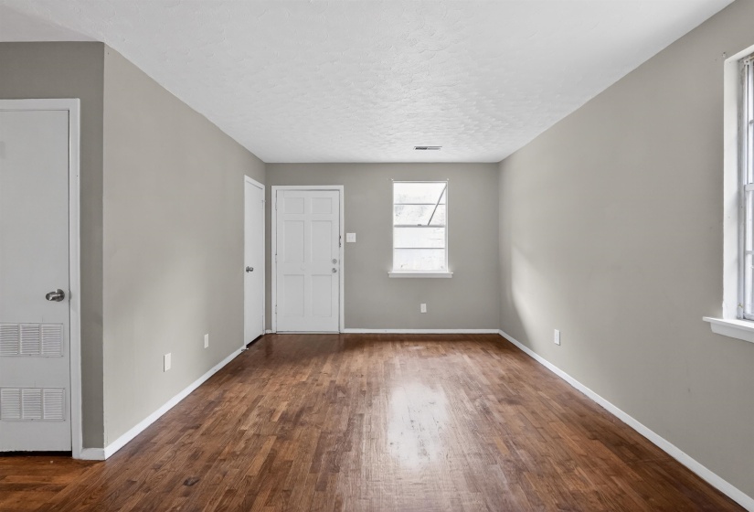 Spacious room featuring wood-finish flooring, light grey walls, white trim, two windows, and multiple white doors
