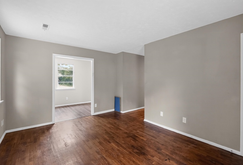 Spacious interior room featuring rich wood-finish flooring, neutral wall tones, and white baseboards