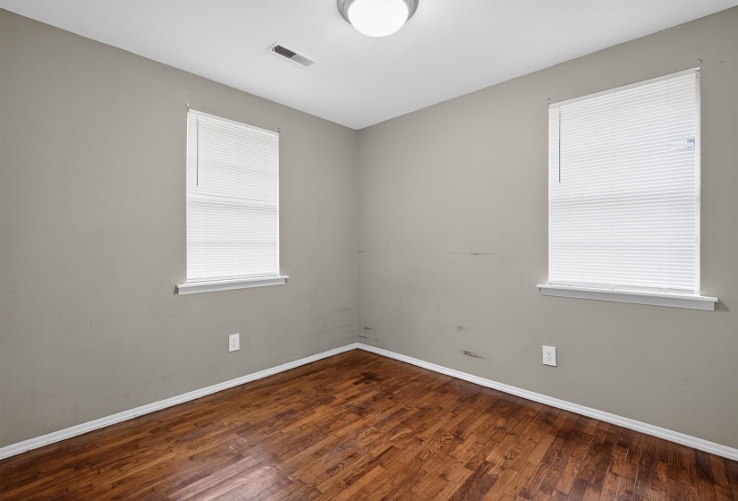 Room featuring wood-finish flooring, two windows with blinds, a ceiling-mounted light fixture, and a white baseboard trim