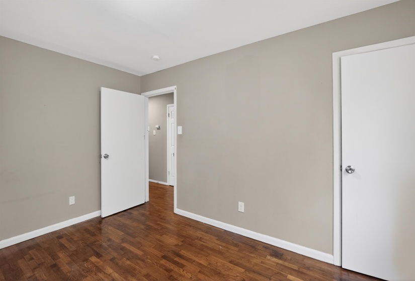 Room featuring wood-finish flooring, neutral wall paint, white trim, and two white doors with silver-tone hardware
