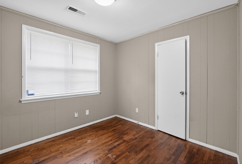 Interior room featuring wood-finish flooring, vertical paneling on walls, a bright window with blinds, and a white door with a round knob