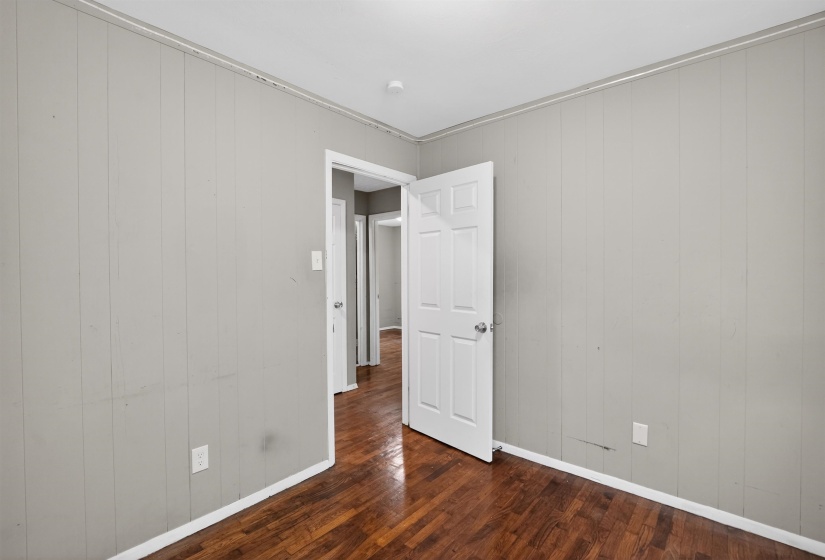 Hardwood flooring throughout, vertical plank wall paneling, white trim work, and a four-panel interior door