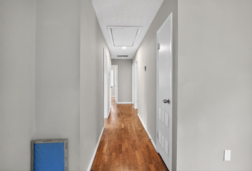 Hallway featuring wood-finish flooring, light gray wall paint, white baseboards, and white interior doors