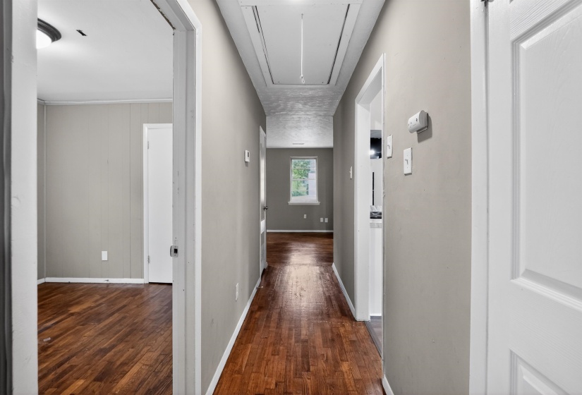 Central hallway featuring wood-finish flooring, light neutral wall paint, white trim, and recessed ceiling access
