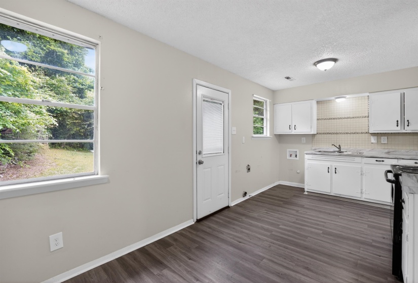 Bright kitchen space featuring wood-finish flooring, white cabinetry, a tiled backsplash, and direct outdoor access