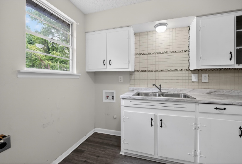 Compact kitchen area featuring white cabinetry, a double basin stainless steel sink, and a light-toned patterned backsplash