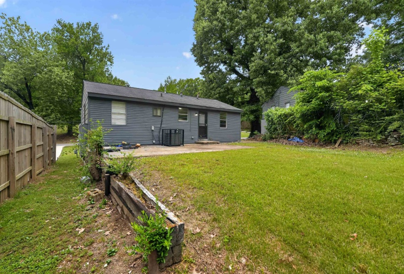 Expansive backyard featuring a manicured lawn, a wooden privacy fence, a concrete patio, and a raised garden bed constructed from railroad ties