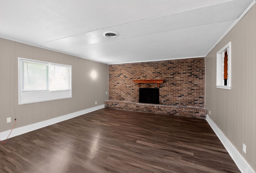 Spacious interior featuring wood-finish flooring, a brick-faced fireplace with a wood mantle, and light-toned paneled walls
