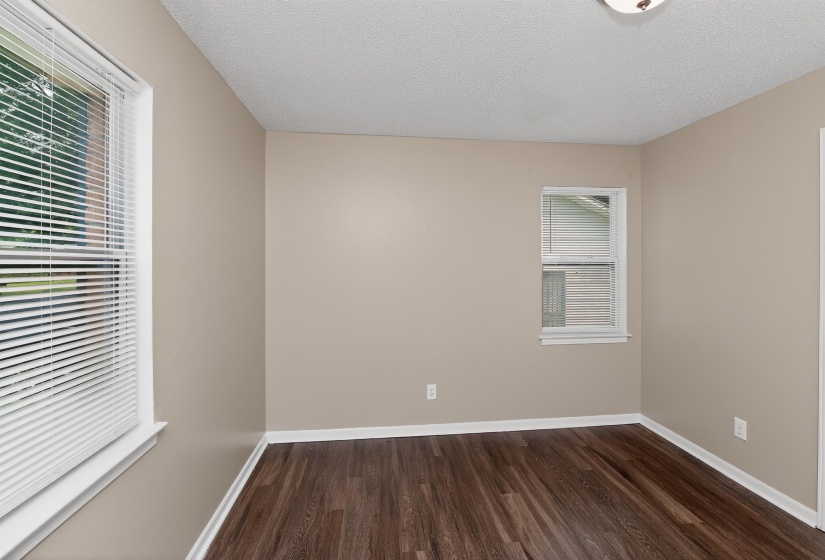 Spacious room featuring wood-finish flooring, two windows with white blinds, and a neutral wall color