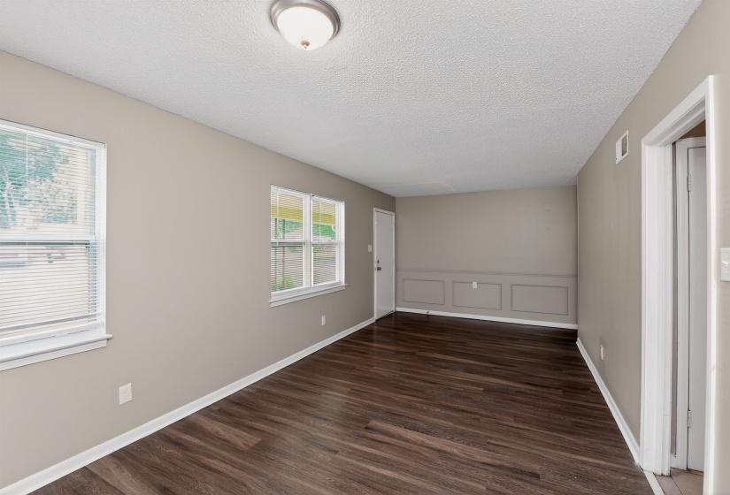 Spacious room featuring wood-finish flooring, neutral-toned walls, multiple windows for natural light, white trim, and decorative wall paneling