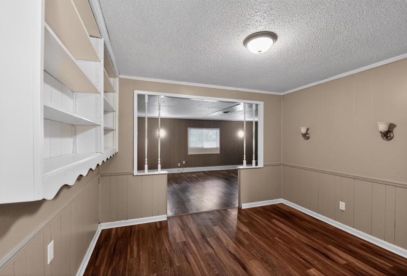 Room featuring wood-finish flooring, built-in shelving, wainscoting, and an archway opening to another room