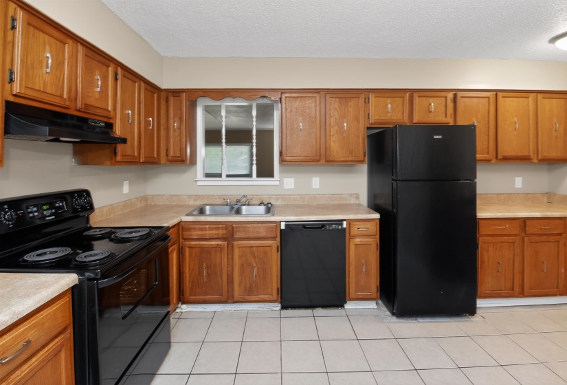 Kitchen featuring wood cabinetry, black appliances, a double basin stainless steel sink, and light-toned countertops
