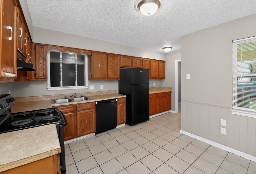 Kitchen featuring wood cabinetry, tiled flooring, black appliances, a double basin stainless steel sink, and a window with blinds
