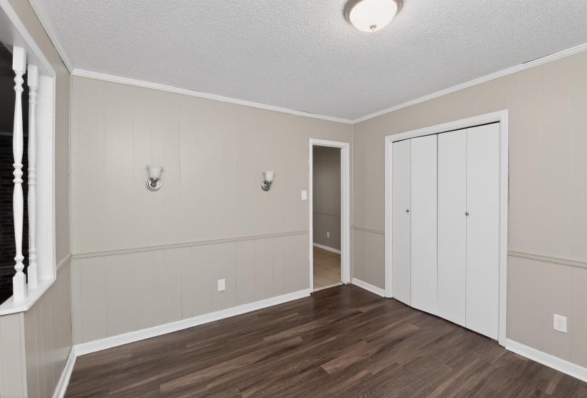 Interior room featuring wood-finish flooring, two-tone wall paneling with chair rail, and a bi-fold door closet