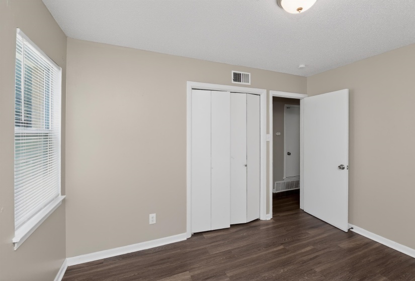 Room featuring wood-finish flooring, a window with blinds, a bi-fold closet, and neutral-toned walls
