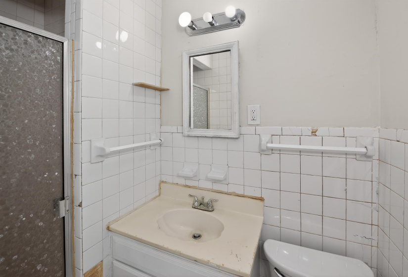 Bathroom featuring white square tile walls, a vanity with an integrated sink, and a framed mirror with overhead lighting