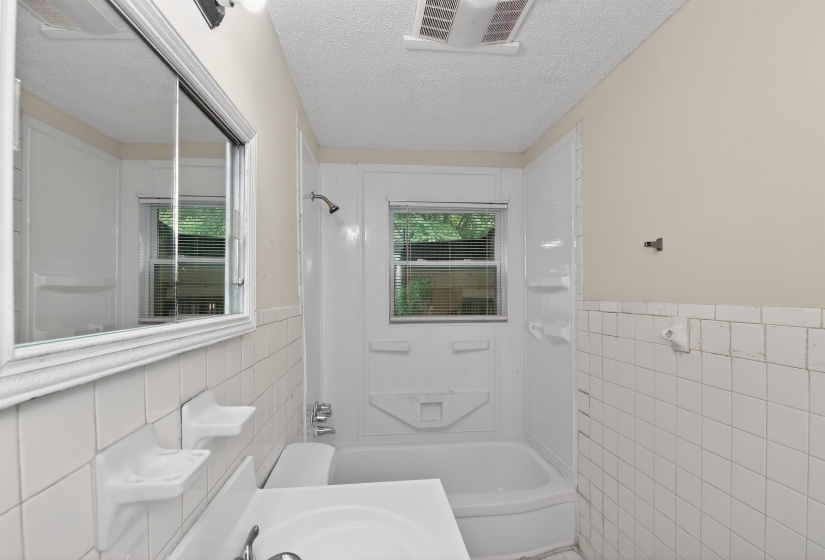 Bathroom featuring white tiled walls, a bathtub with a shower kit, and a window with horizontal blinds