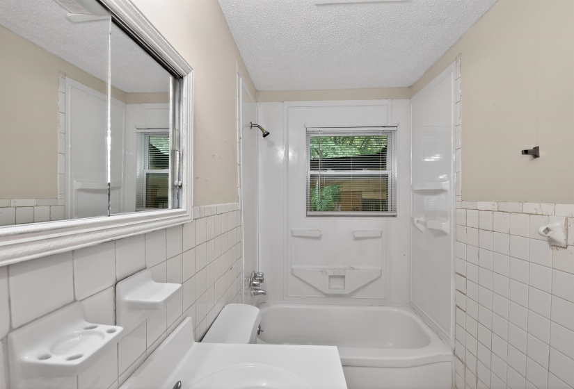 Bathroom featuring a bathtub with an integrated shower, white subway tile wainscoting, and a wall-mounted medicine cabinet