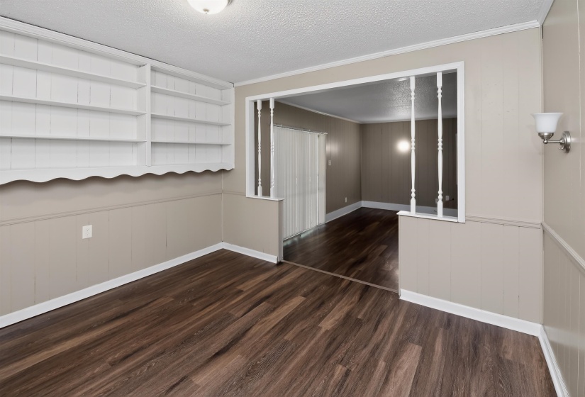 Spacious room featuring wood-finish flooring, wainscoting, and an open doorway with decorative balusters
