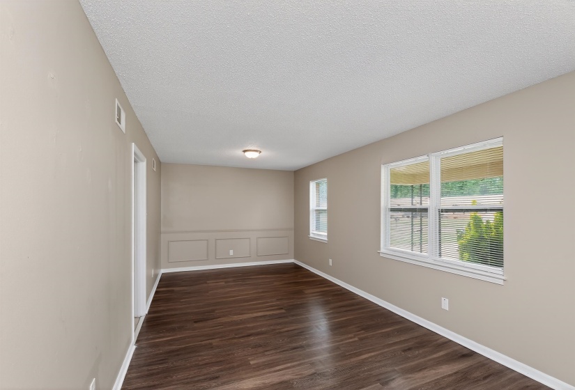 Spacious interior featuring wood-finish flooring, two large windows with blinds, and decorative wainscoting