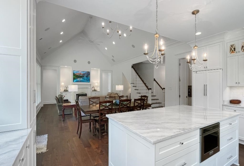 Gourmet kitchen with a large central island featuring a built-in microwave, white shaker cabinetry, and light-toned stone countertops