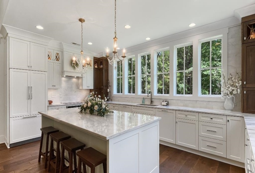Kitchen featuring a large central island with seating, white cabinetry, integrated refrigerator, and light-toned countertops