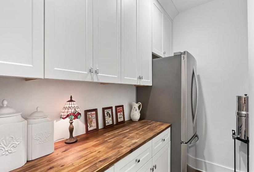 White shaker-style cabinetry with silver hardware, wood-finish countertops, and a stainless steel refrigerator