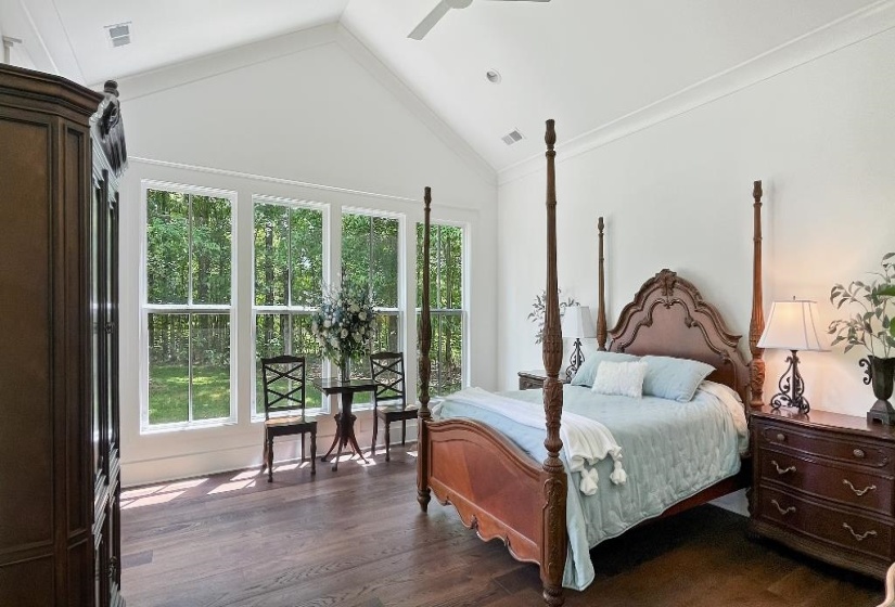 Bedroom featuring vaulted ceilings, wood-finish flooring, and a wall of three large windows providing abundant natural light