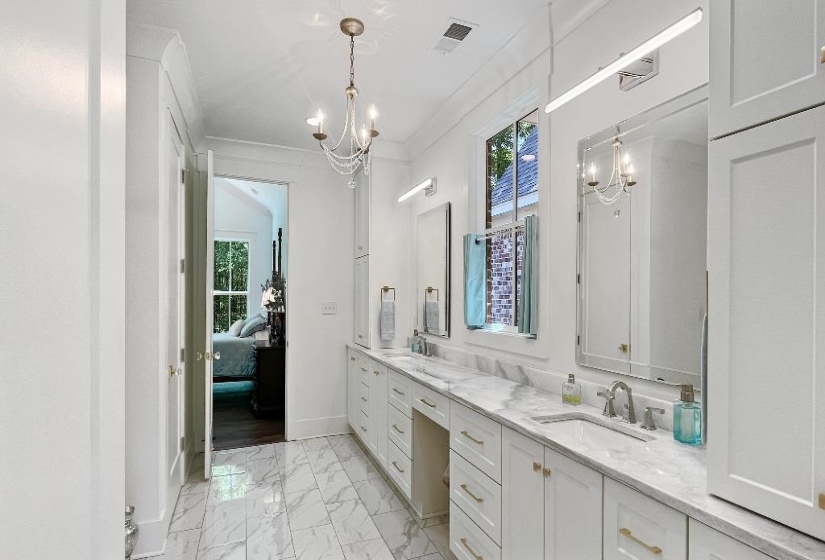 Spacious bathroom featuring marble-finish tile flooring, a dual vanity with white cabinetry and gold-tone hardware, and a white marble-finish countertop