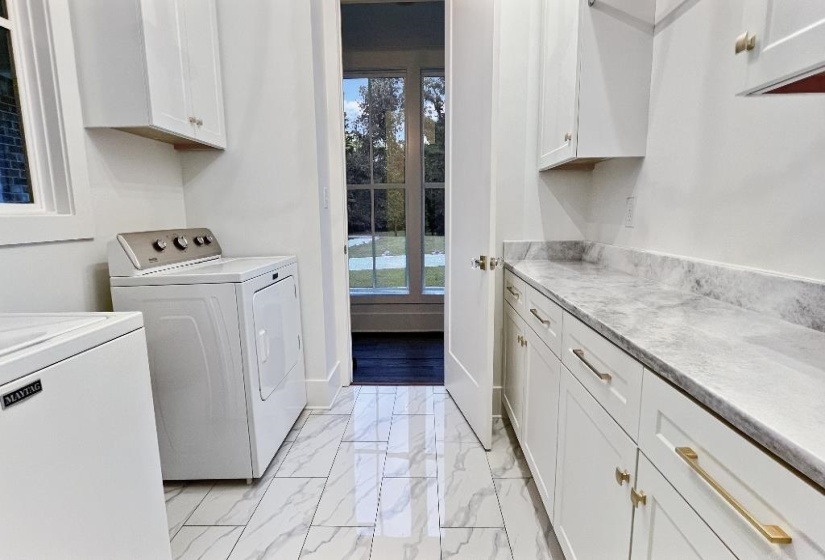 Laundry area featuring white cabinetry, light-toned countertops, and marble-look tile flooring