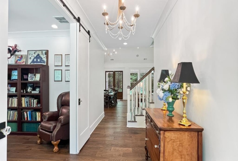Spacious hallway with wood-finish flooring, a decorative chandelier, and white wall paneling