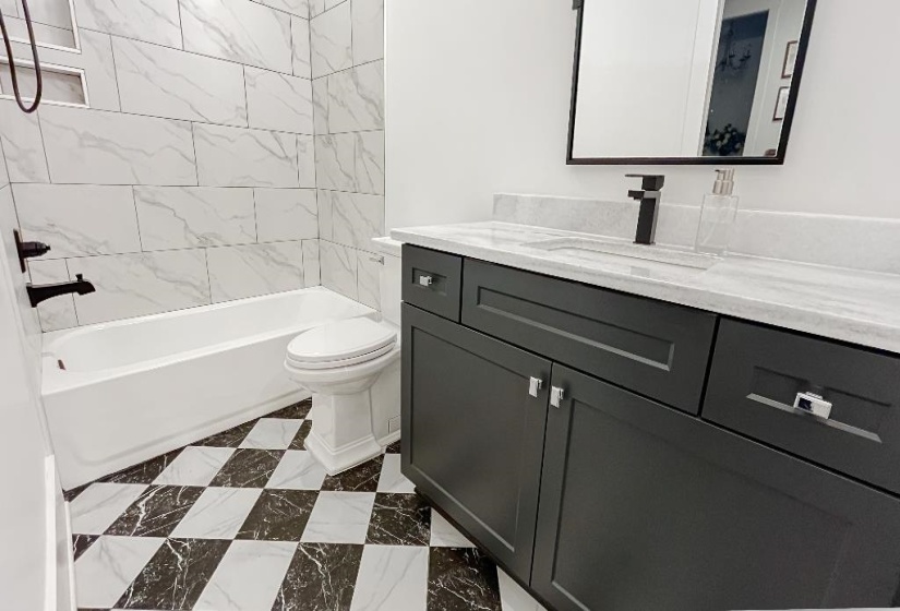 Bathroom featuring a checkered floor, white bathtub, and a dark gray vanity with a light countertop