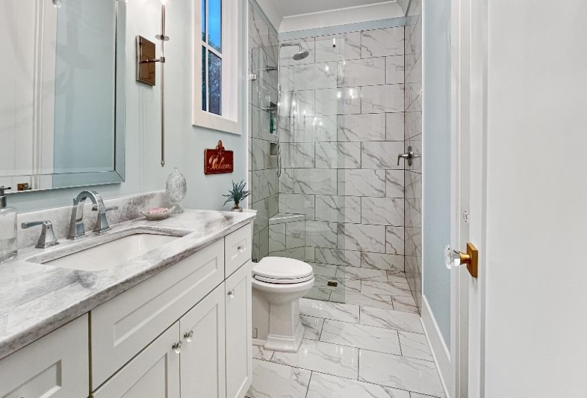 Bathroom featuring a white vanity with crystal knobs, a rectangular undermount sink, a stone-finish countertop, and a walk-in shower with glass enclosure and large format tile
