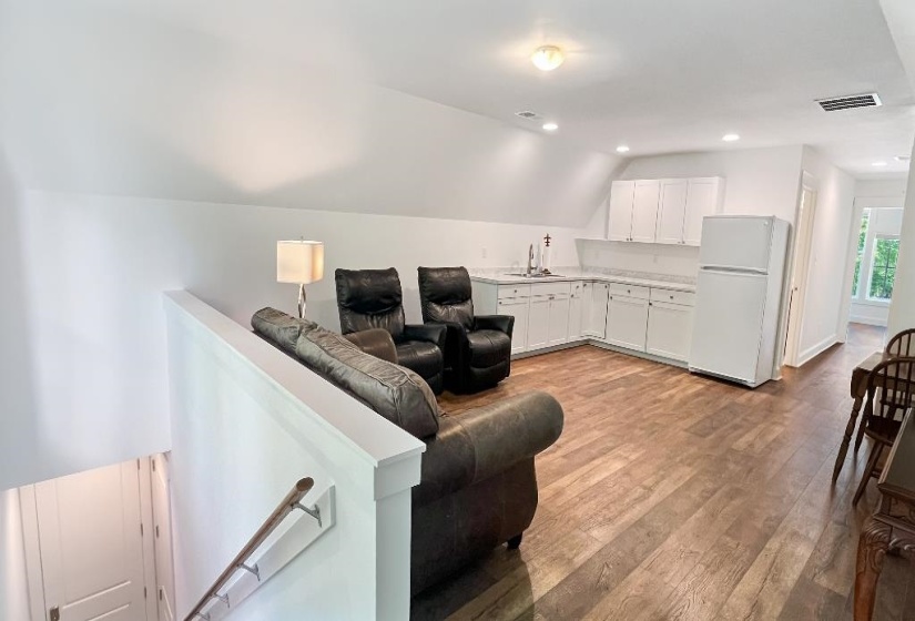 Open-concept space featuring wood-finish flooring, a white L-shaped kitchen area with base and upper cabinetry, and a white refrigerator
