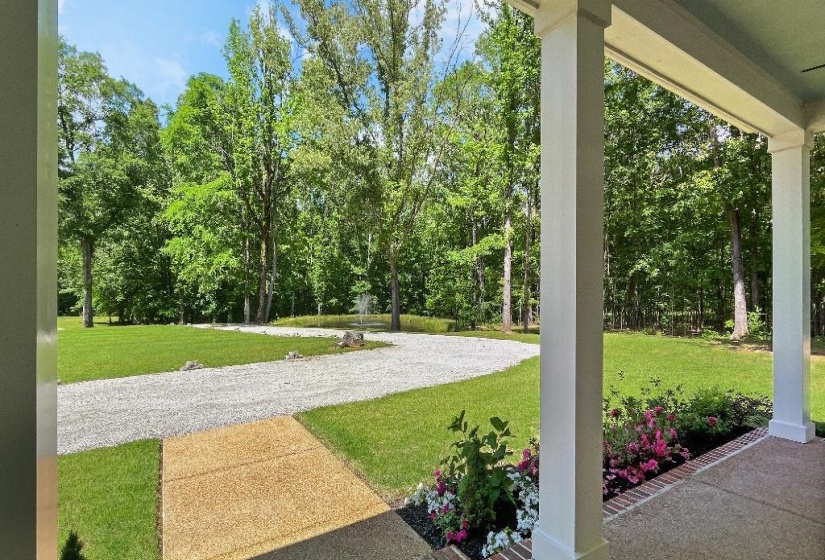 Covered porch with white columns, concrete flooring, and an adjacent landscaped planting bed with flowering shrubs