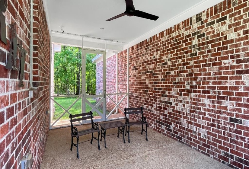 Screened outdoor living area featuring brick walls with white mortar, a dark-toned ceiling fan, and a speckled concrete floor