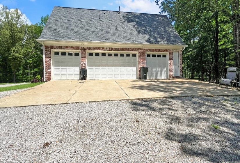 Detached brick garage structure featuring three individual bays with white paneled doors, a gray shingle roof, and an additional side entry door