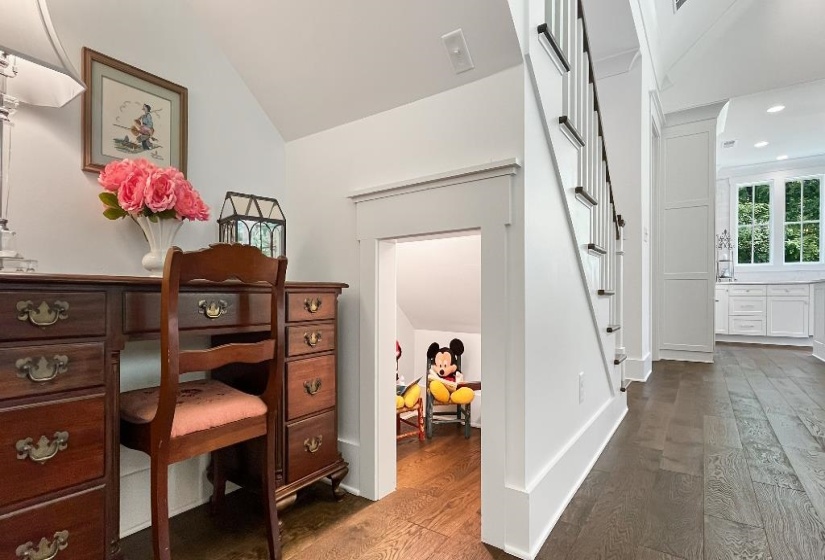 Hardwood flooring extending through the hallway, staircase with white risers and dark handrails, and a dedicated under-stair alcove
