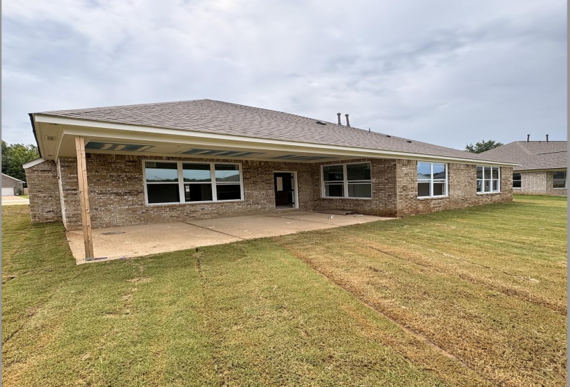 Rear exterior featuring a covered patio, brick facade, numerous windows, and a shingle roof