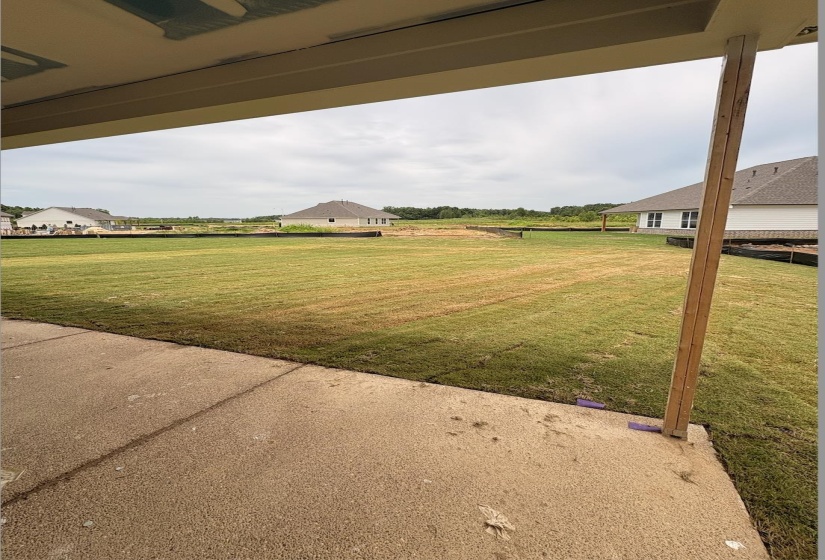 Spacious concrete patio overlooking an expansive lawn with a backdrop of green space and distant residential structures