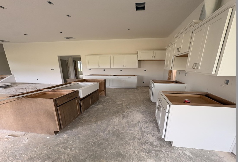 Spacious kitchen featuring white shaker-style perimeter cabinetry, a large kitchen island with a farmhouse sink, and recessed lighting pre-installations