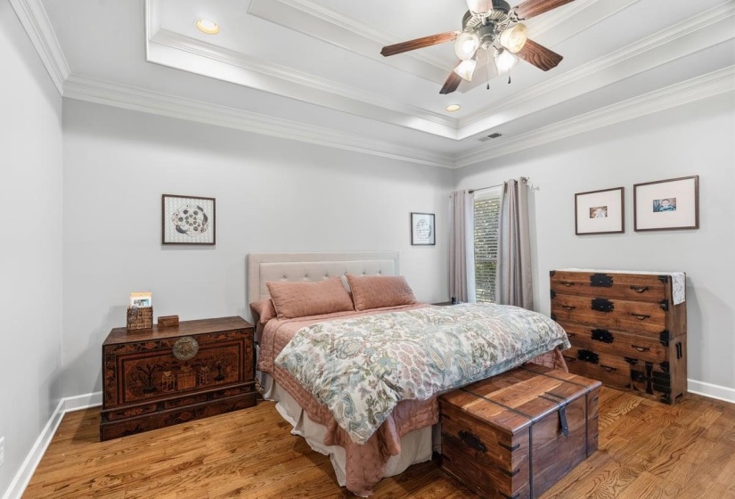 Primary Bedroom featuring hardwood flooring, a tray ceiling with recessed lighting, and a ceiling fan