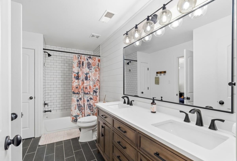 Updated Bathroom featuring a dual vanity with a white countertop and matte black fixtures, set against a shiplap accent wall